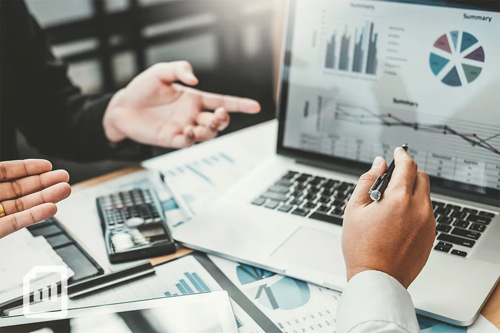hands gesturing and pointing at a computer showing financial charts